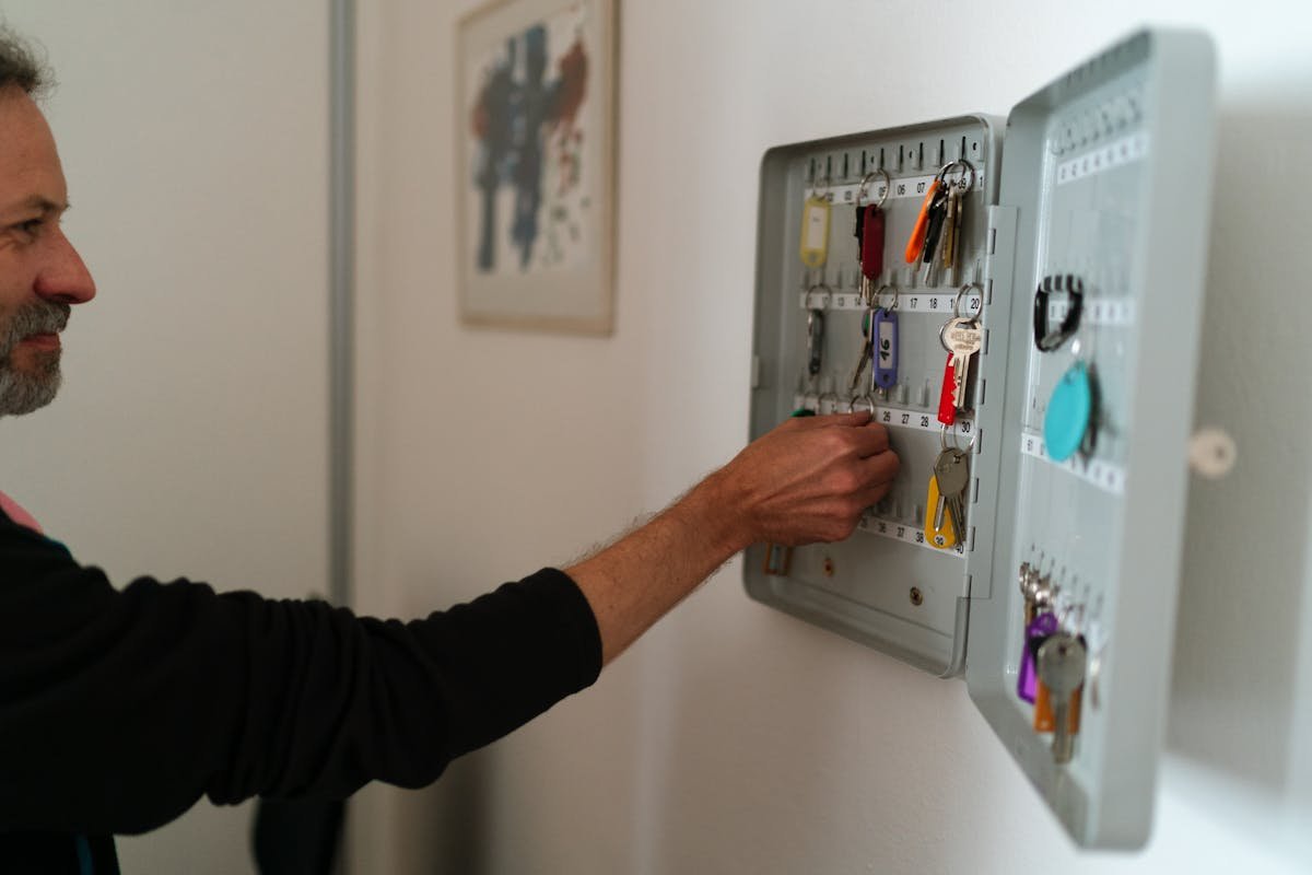 Síndico profissional e a segurança no condomínio: funções e estratégias A man arranges keys in a wall-mounted cabinet inside an office setting.