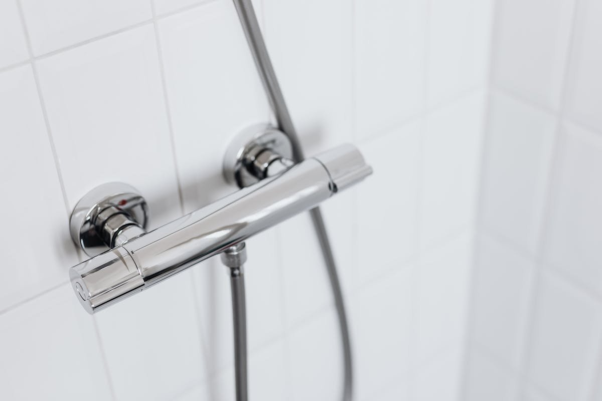 Prevenindo acidentes com sistemas hidráulicos entupidos Modern chrome shower faucet on white tiled wall, elegant and clean design.