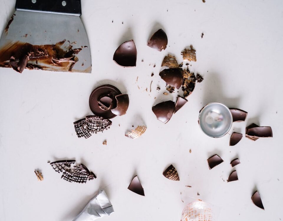 Dicas de segurança para fazer doces artesanais em casa Flatlay of chocolate pieces and a scraper on a white surface, perfect for confectionery themes.