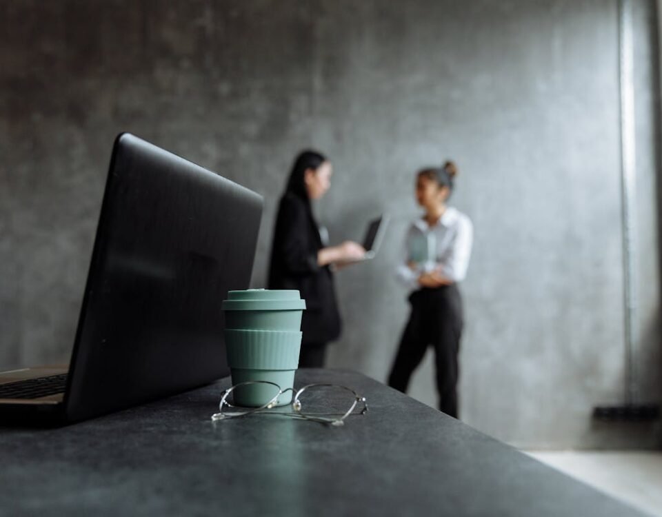 Os 5 maiores erros no controle de ponto e como evitá-los Two professionals discuss business strategies in a stylish office setting with a focus on a laptop and glasses.