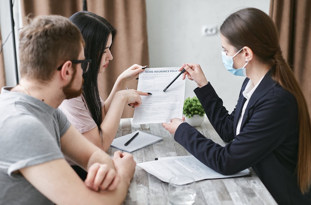 Seguro residencial: vale a pena incluir itens de valor? Three adults discuss a home insurance policy at a meeting table indoors.