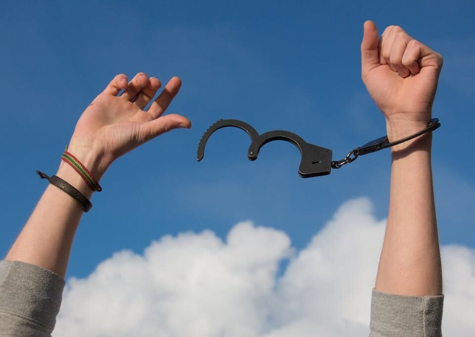 Regime aberto: O que advogados criminalistas explicam sobre a segurança Symbolic image of freedom with open handcuffs against a bright blue sky.
