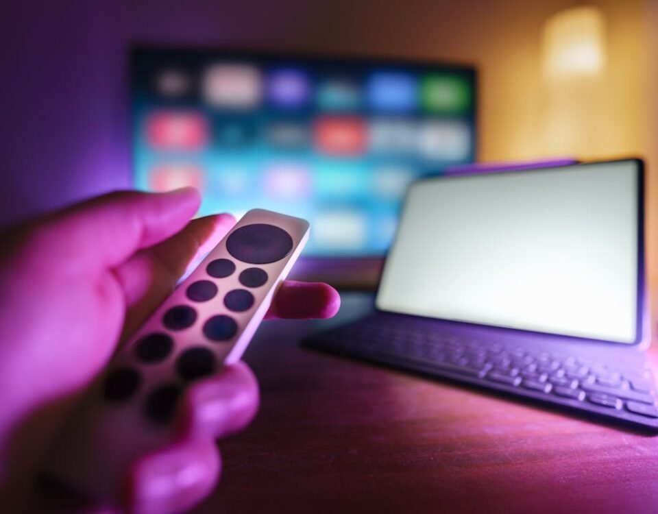 Segurança digital ao assistir filmes online A hand using a remote to control a TV and laptop in a cozy room setting, perfect for relaxation.