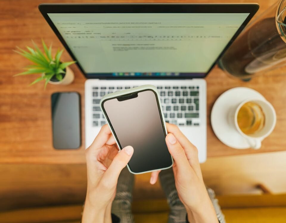 Como proteger sua privacidade ao acessar notícias online Hands holding a smartphone over a laptop with coffee in a cozy home office setup.