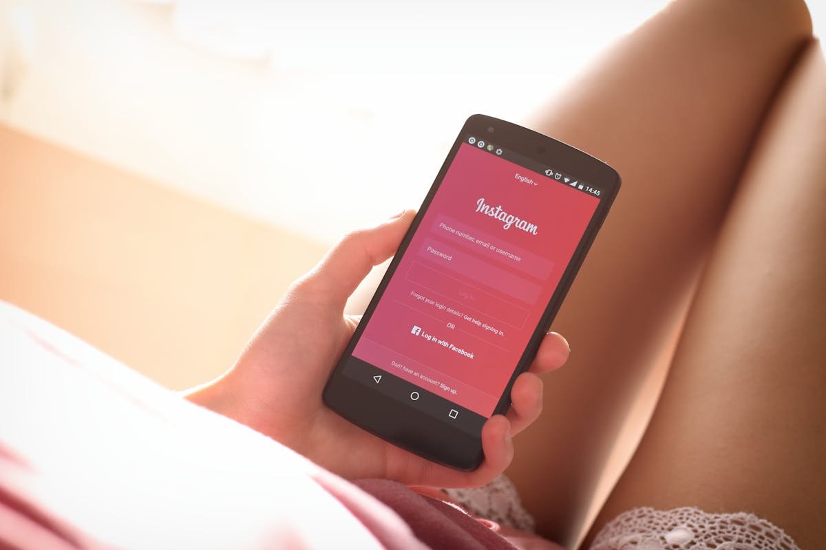 Privacidade no Instagram: Proteja sua casa nas redes Woman holding a smartphone with Instagram login screen while relaxing indoors.