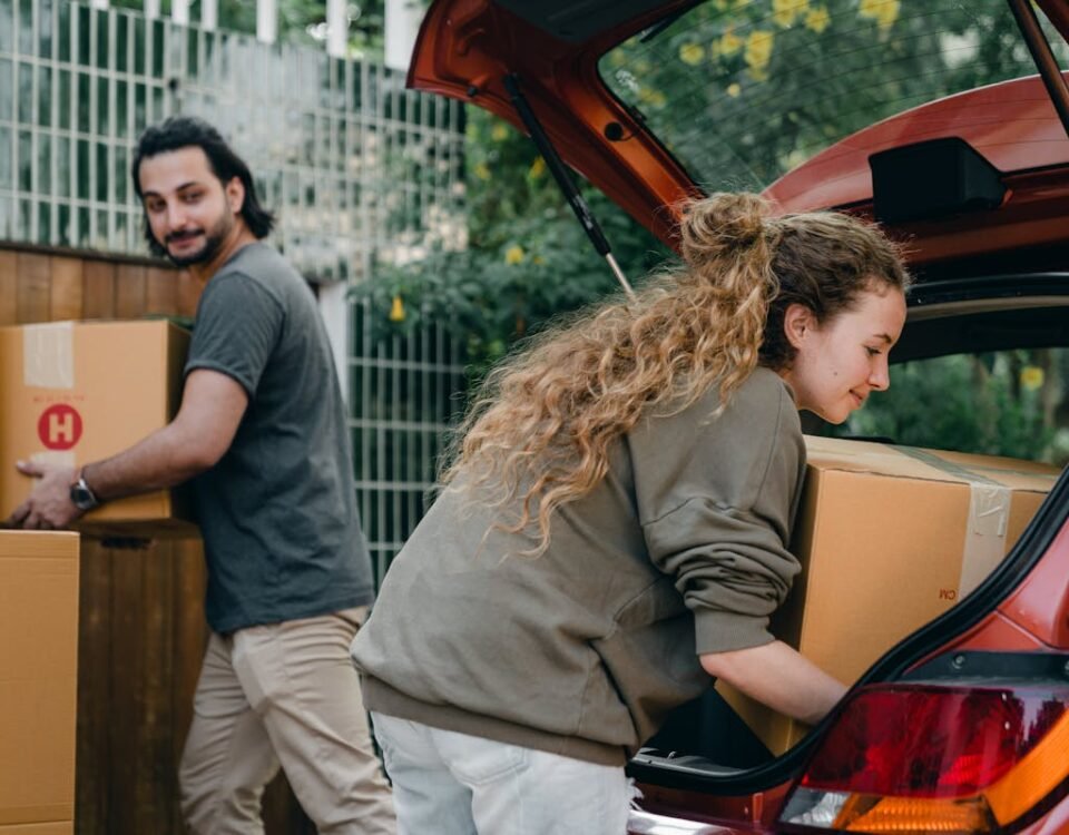 Proteção total: Como unir seguro auto e residencial? Positive multiethnic boyfriend and girlfriend unloading car trunk during moving to new home in quiet green yard on summer day