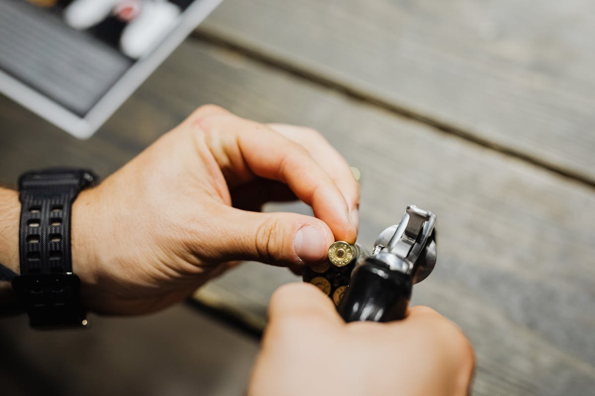 Ter uma arma em casa aumenta a segurança familiar? Close-up of hands loading bullets into a revolver on a wooden surface.