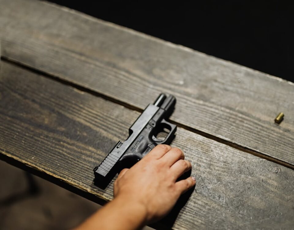 Armas em casa: segurança ou preocupação? Close-up of a hand holding a handgun on a wooden table with bullet casing.