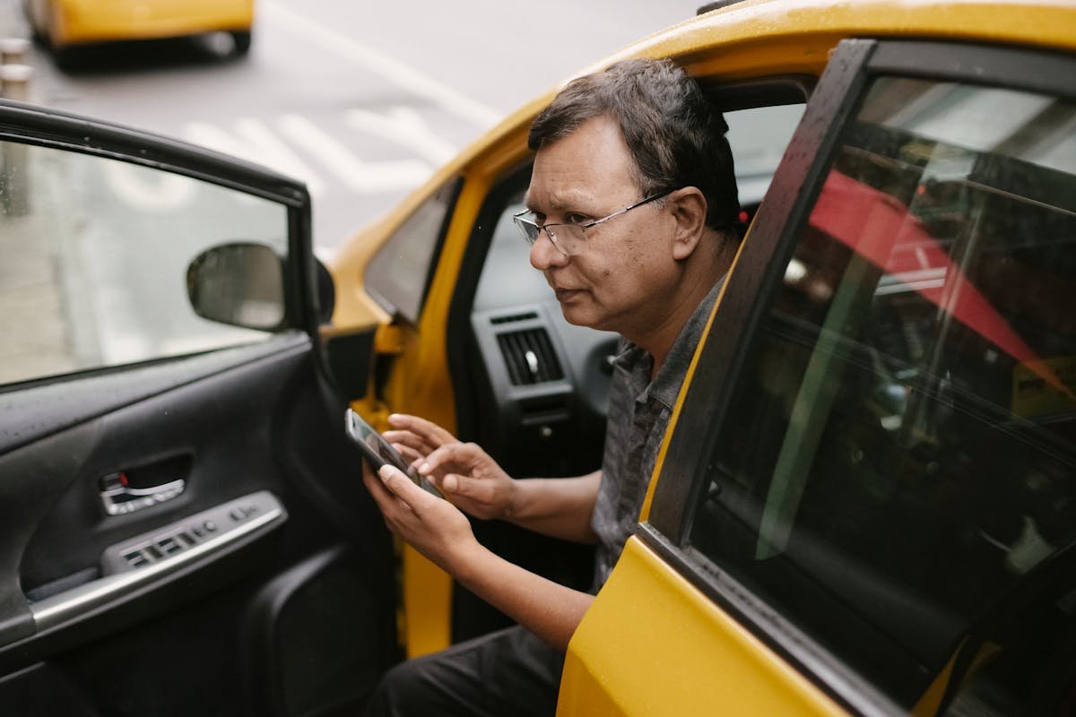 CNH digital: é segura para comprovar sua identidade? Crop Asian man sitting in parked yellow taxi car with open door and using smartphone while looking away