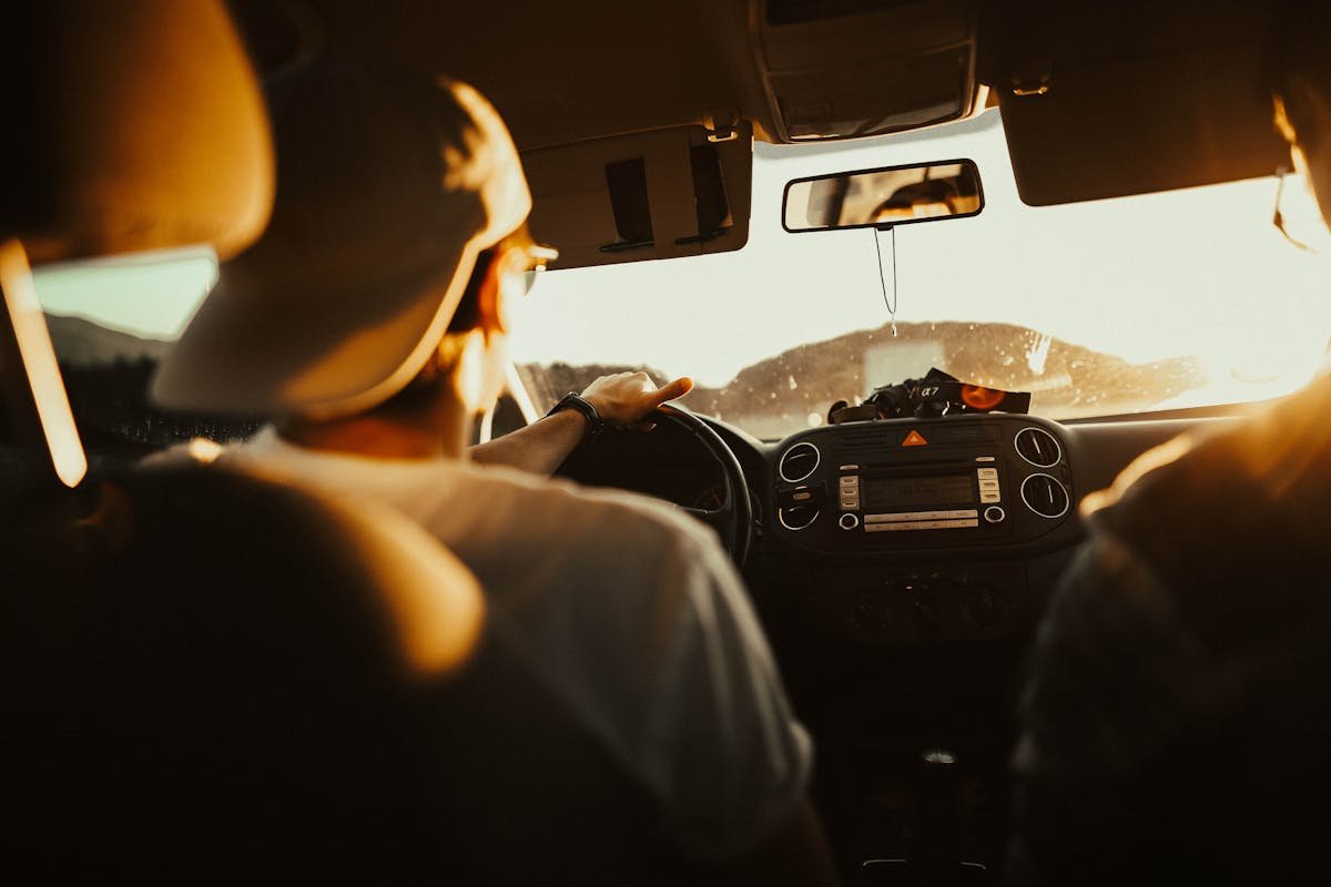 Como proteger seu carro enquanto você aprende a dirigir Man driving car with passenger at sunset, capturing warm sunlit atmosphere.