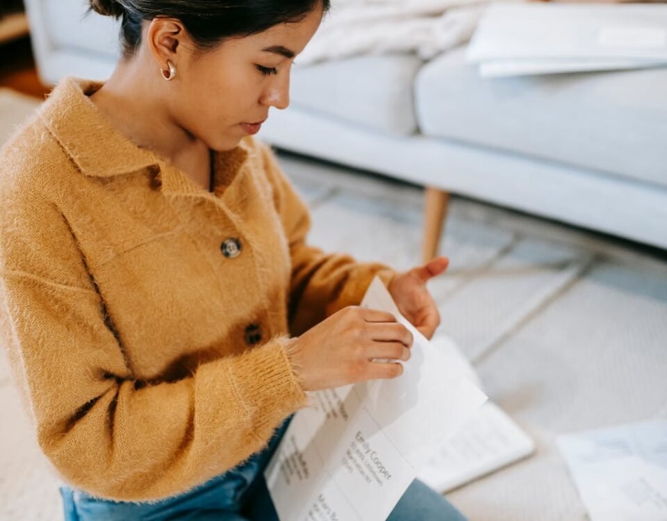 Como evitar multas de trânsito com organização em casa Young woman sitting on the floor reviewing paperwork in a cozy home setting.