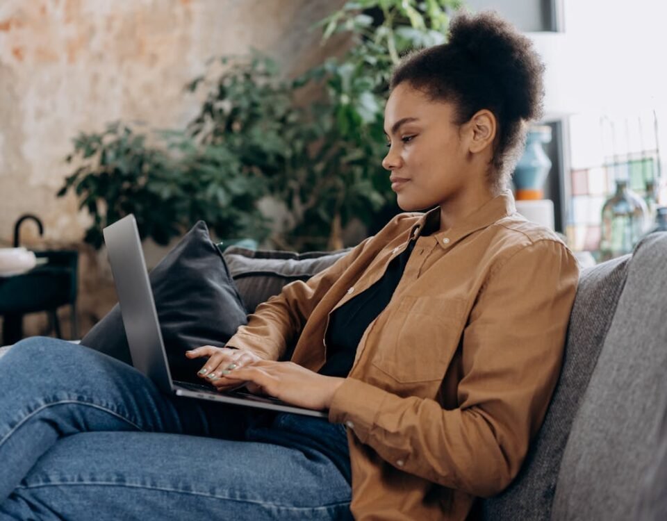Como sites ajudam na organização de um home office seguro A young woman in casual clothing works on her laptop in a cozy home office setting.