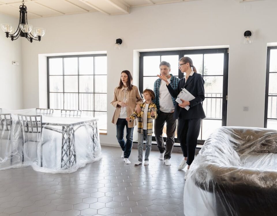 Seguro residencial é obrigatório ao financiar imóveis? A real estate agent tours a family in a newly furnished house, featuring covered furniture.