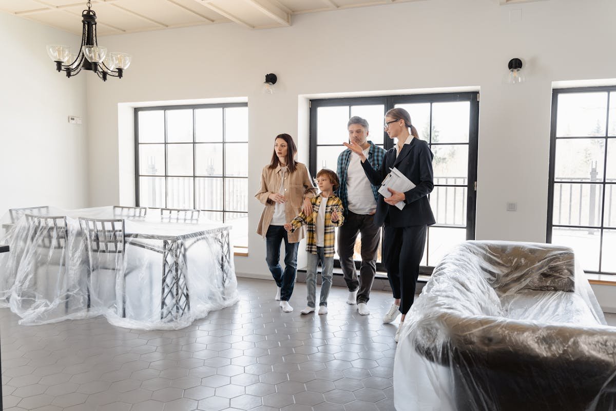 Proteção total: Como unir seguro auto e residencial? A real estate agent tours a family in a newly furnished house, featuring covered furniture.