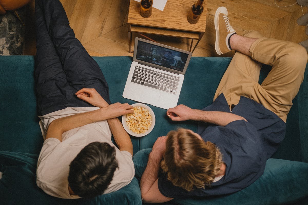 Segurança digital ao assistir filmes online Two friends enjoying a movie on a laptop with popcorn from a cozy couch perspective.