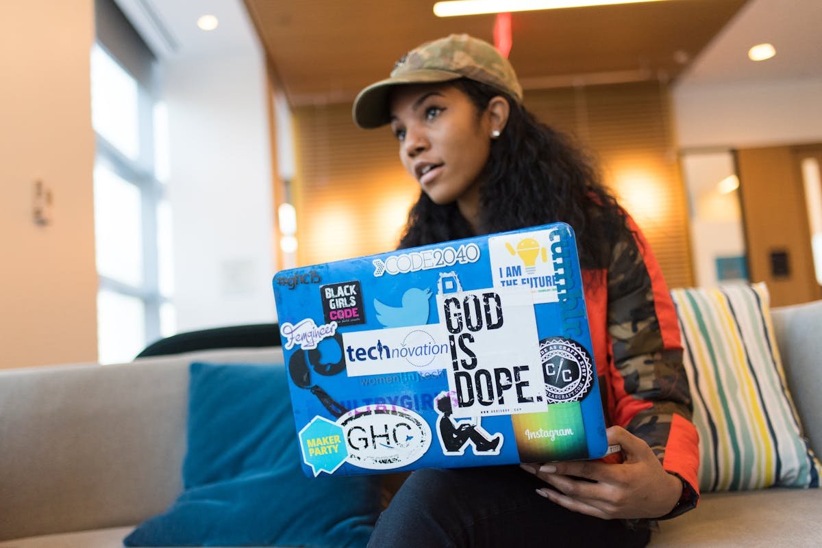 Design criativo no ambiente de trabalho: como pode impactar clientes Tech-savvy woman with sticker-decorated laptop working indoors, showing innovation and creativity.