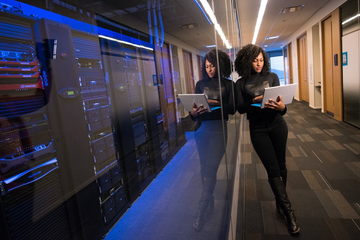 Segurança de dados empresariais começa no escritório A woman using a laptop navigating a contemporary data center with mirrored servers.