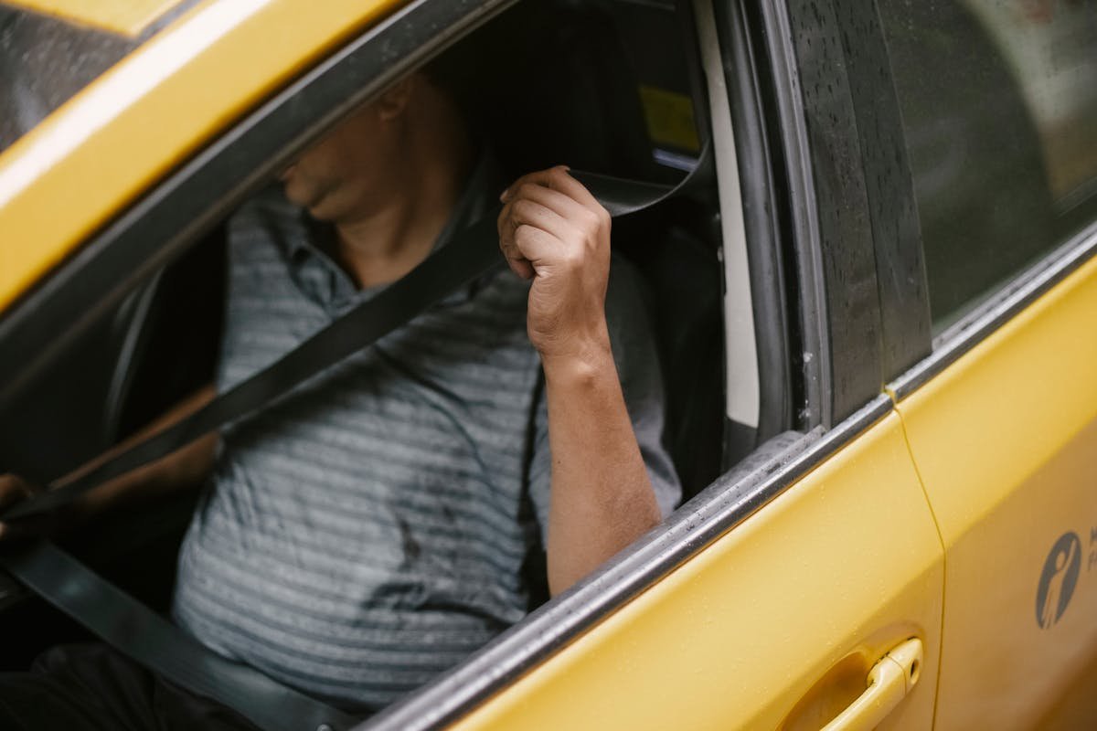 CNH e seguros: O que considerar ao dirigir A man securely fastens his seatbelt inside a yellow taxi, emphasizing safety during urban transport.