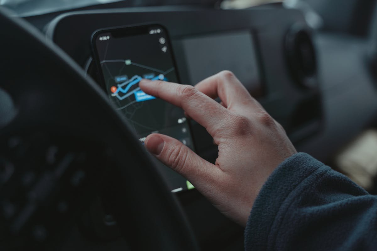 Sistemas de monitoramento veicular para novos motoristas Hand interacting with GPS navigation on a smartphone mounted in a car interior.