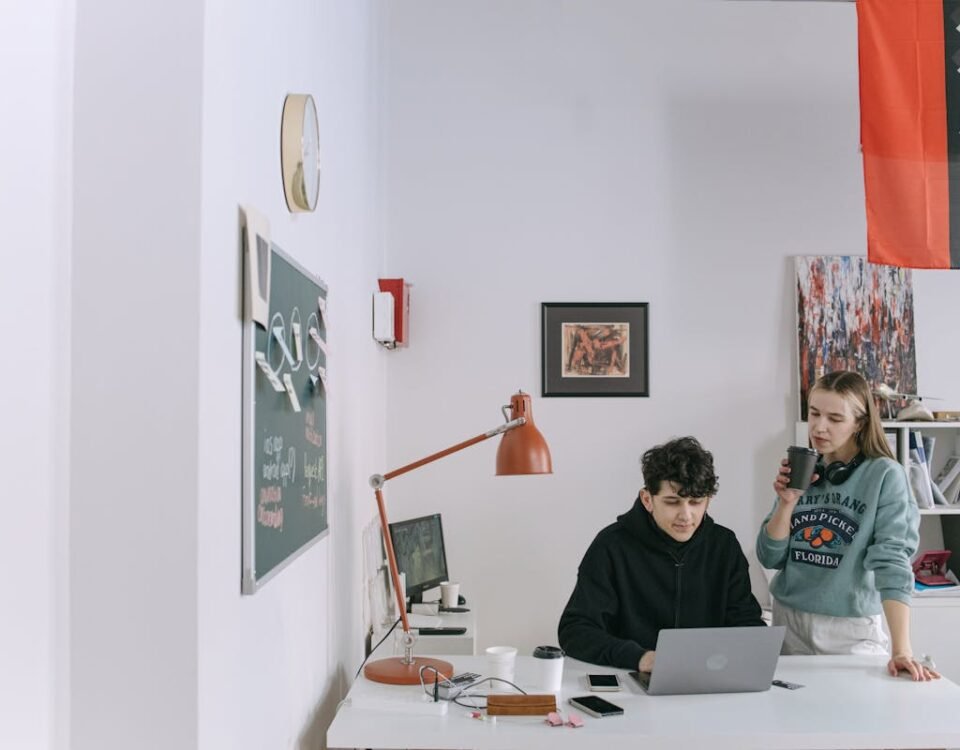 Design criativo no ambiente de trabalho: como pode impactar clientes Two young adults working in a modern office, collaborating on a project with a laptop.