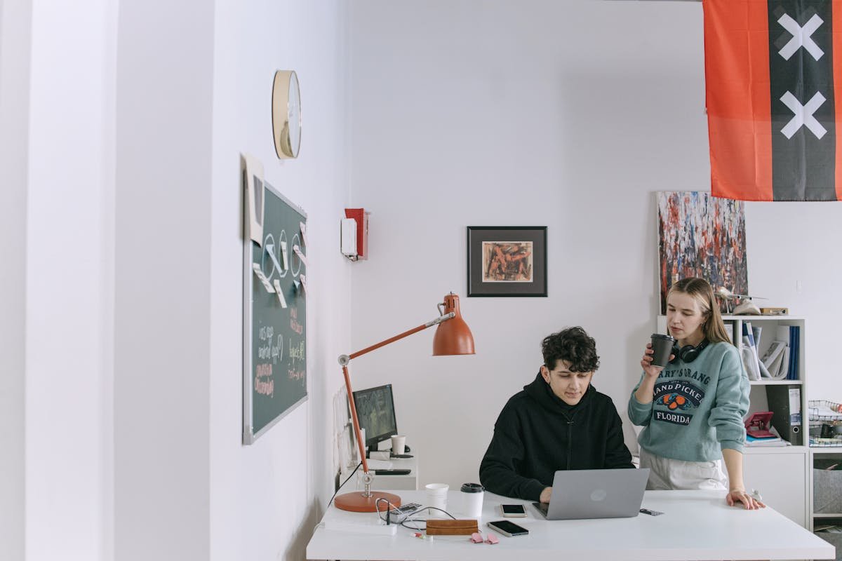 Two young adults working in a modern office, collaborating on a project with a laptop.