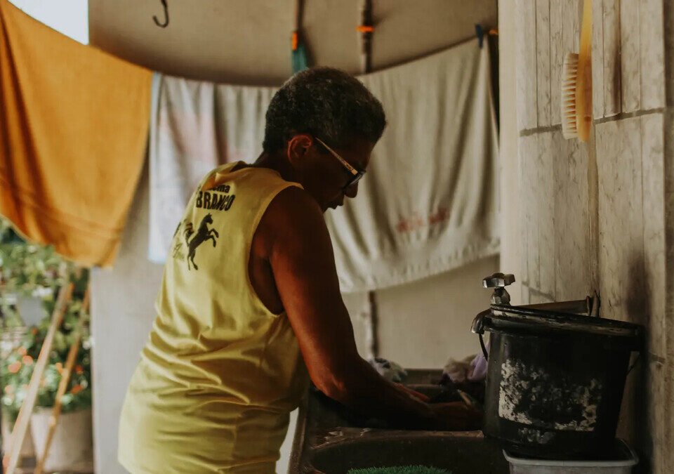Pessoa lava louças em uma cozinha doméstica, em imagem ilustrativa