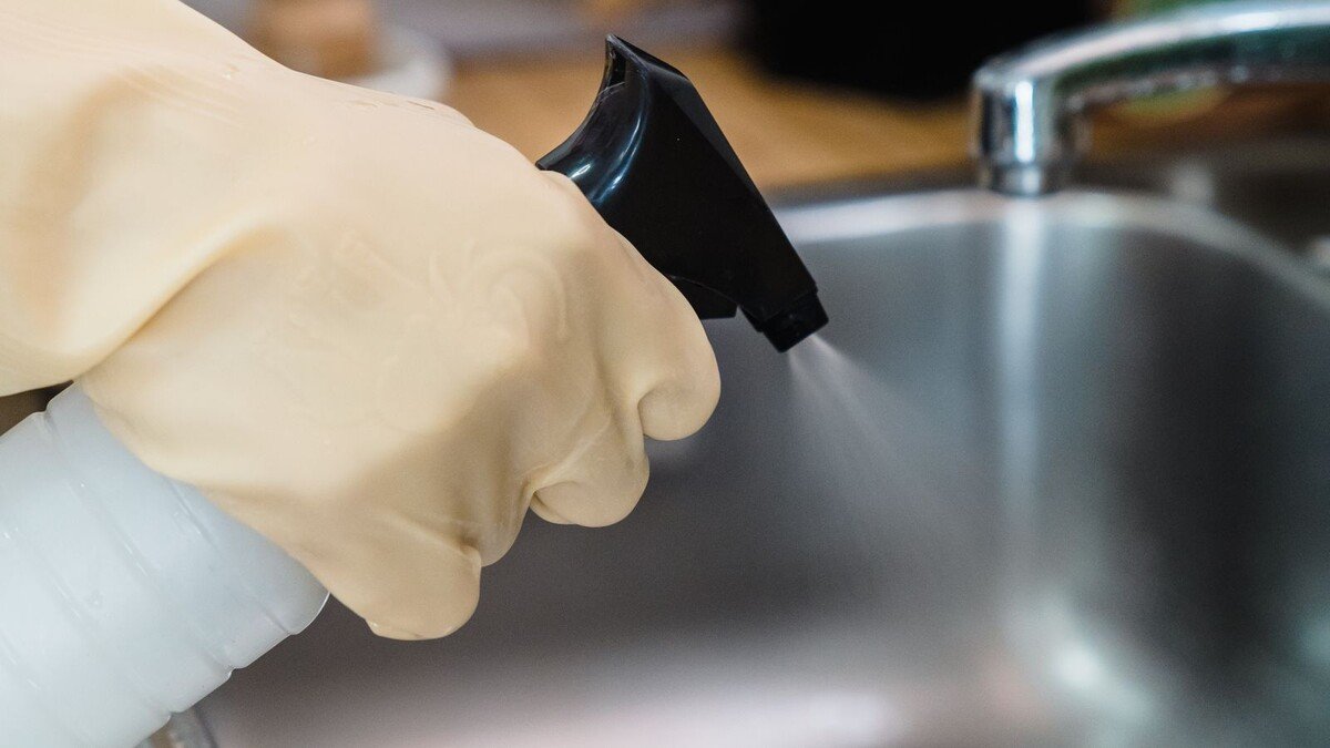 Anvisa libera lotes Ypê de novembro e dezembro de 2025: como conferir Mão com luva de borracha borrifando produto de limpeza em pia de inox