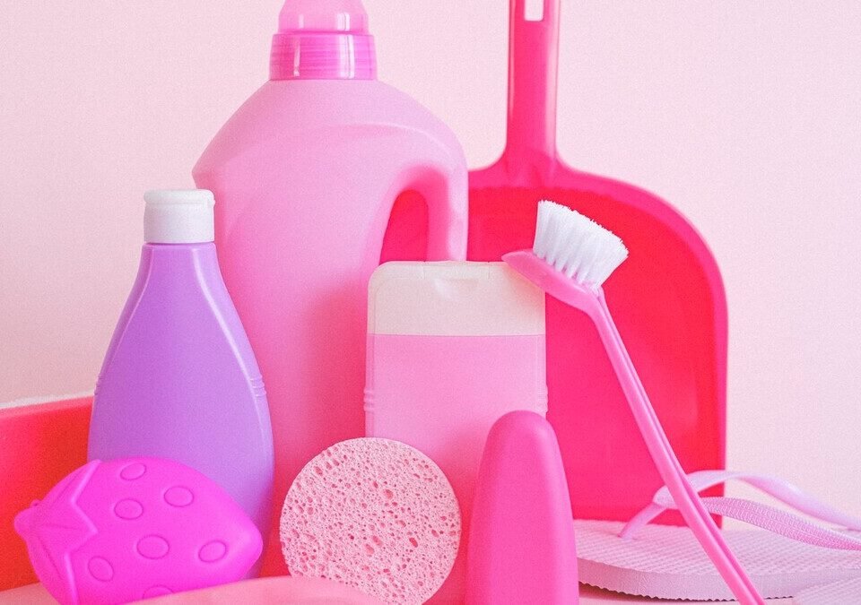 Frascos de produtos de limpeza sem marca, esponjas e escova em fundo rosa