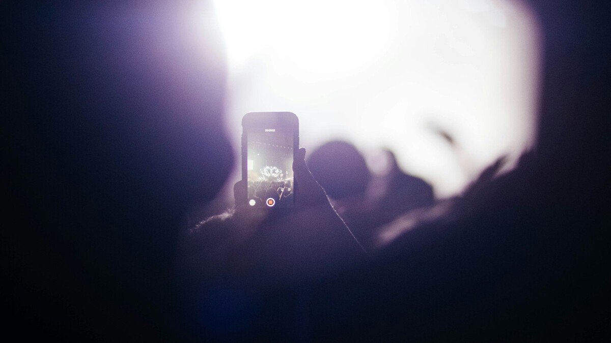 Pessoa segurando um smartphone preto gravando vídeo em ambiente escuro