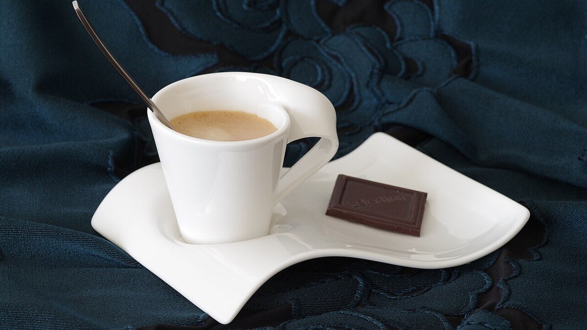 Cantinho do café pequeno: o que realmente vale ter em casa? Xícara branca de café com pires e um pedaço de chocolate