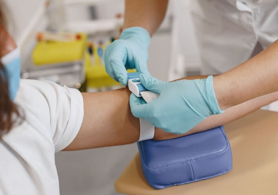 Profissional de saúde preparando o braço de um paciente apoiado em uma almofada para coleta de sangue
