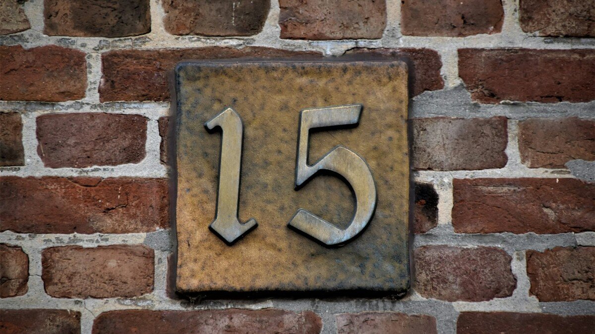 Número e nome na fachada de casa: qual material dura mais? Placa metálica com o número 15 em relevo presa a parede de tijolos