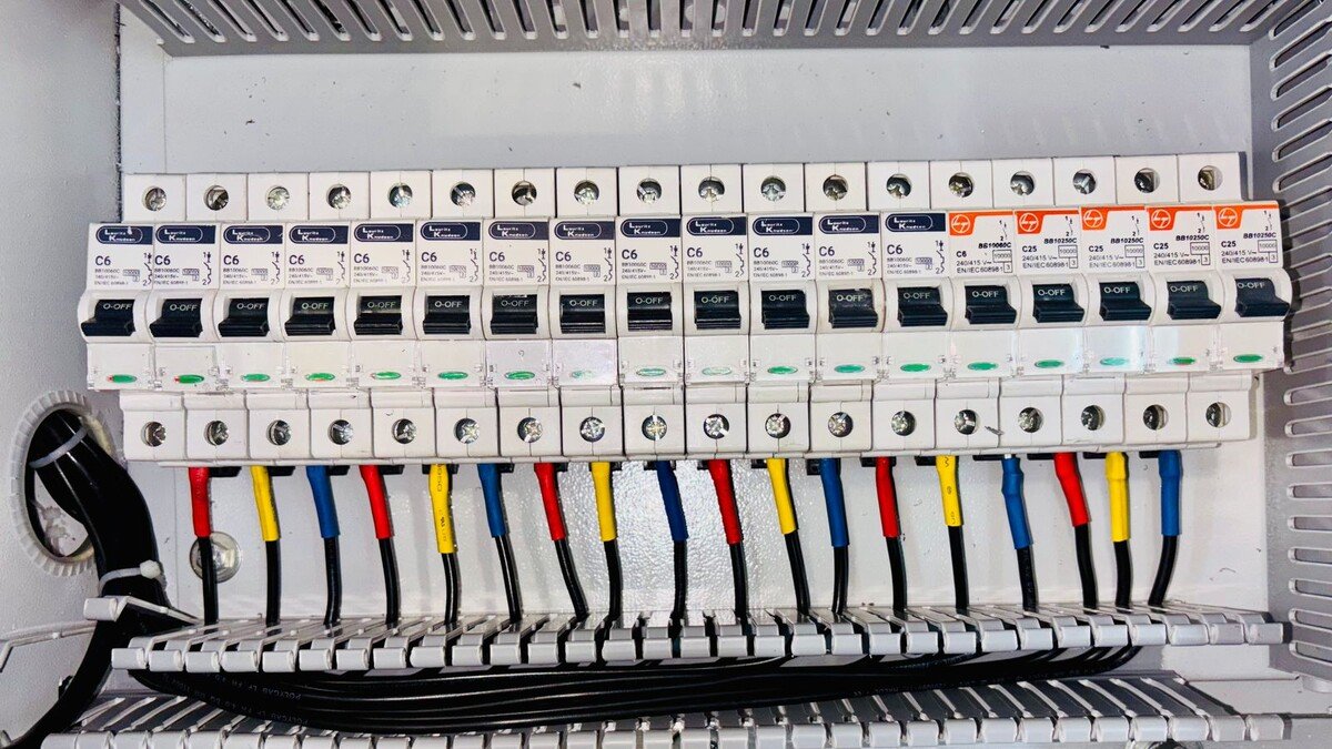 Fileira de disjuntores em quadro de distribuição elétrica com fios coloridos
